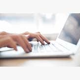 Close-up of male hands typing on laptop keyboard indoors. Businessman working in office or student browsing information